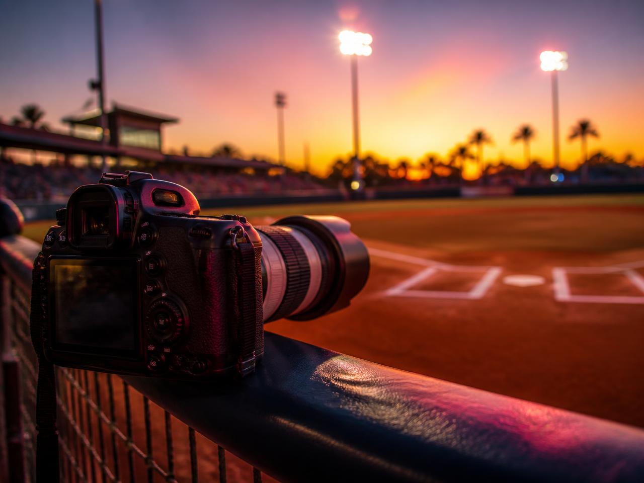 Camera with telephoto lens on a dugout rail overlooking a softball field at sunset